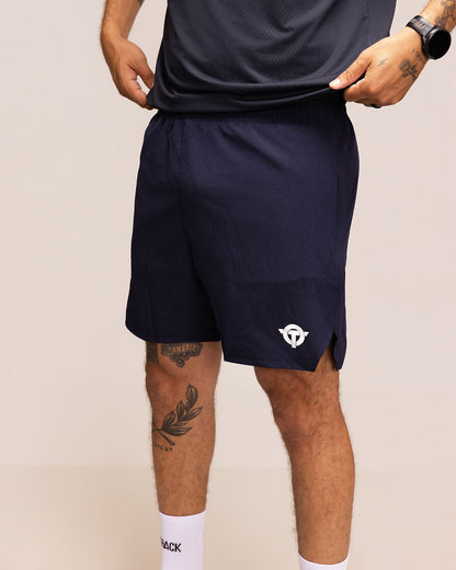 Person wearing navy athletic shorts with a logo on a beige background