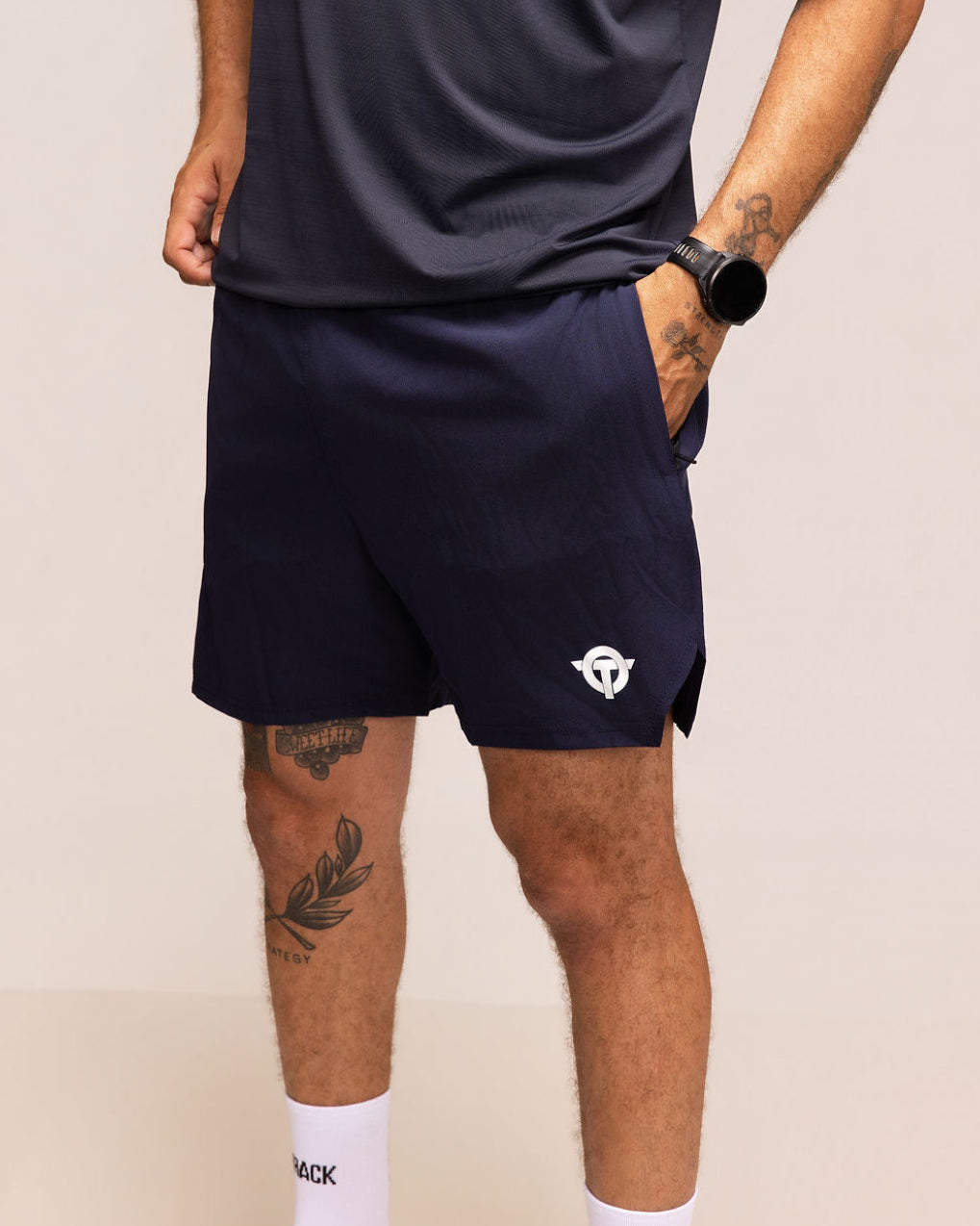 Person wearing navy athletic shorts with a logo on a beige background